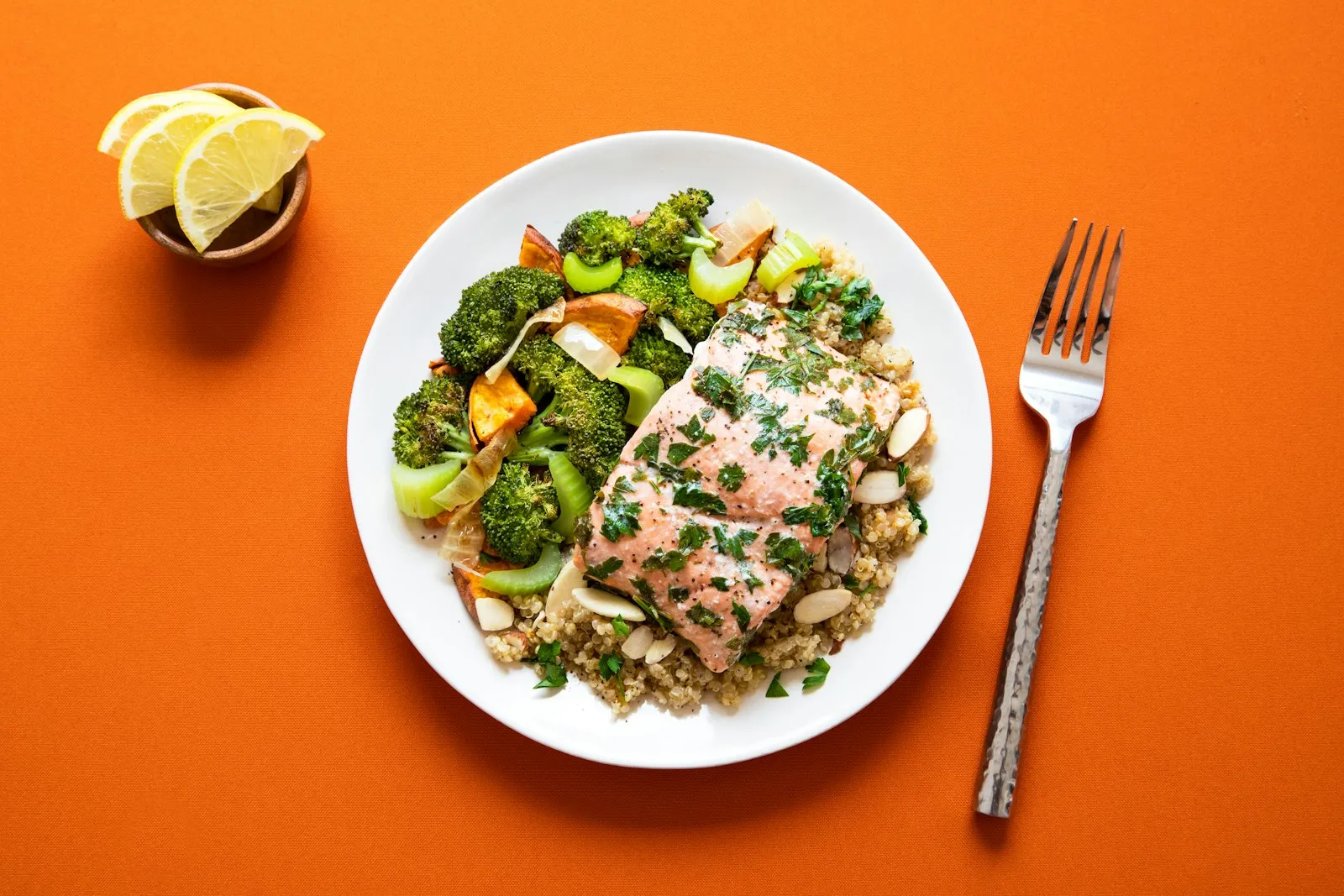Vue du dessus d'une assiette de saumon cuit sur du quinoa, avec du brocoli rôti, sur un fond orange.